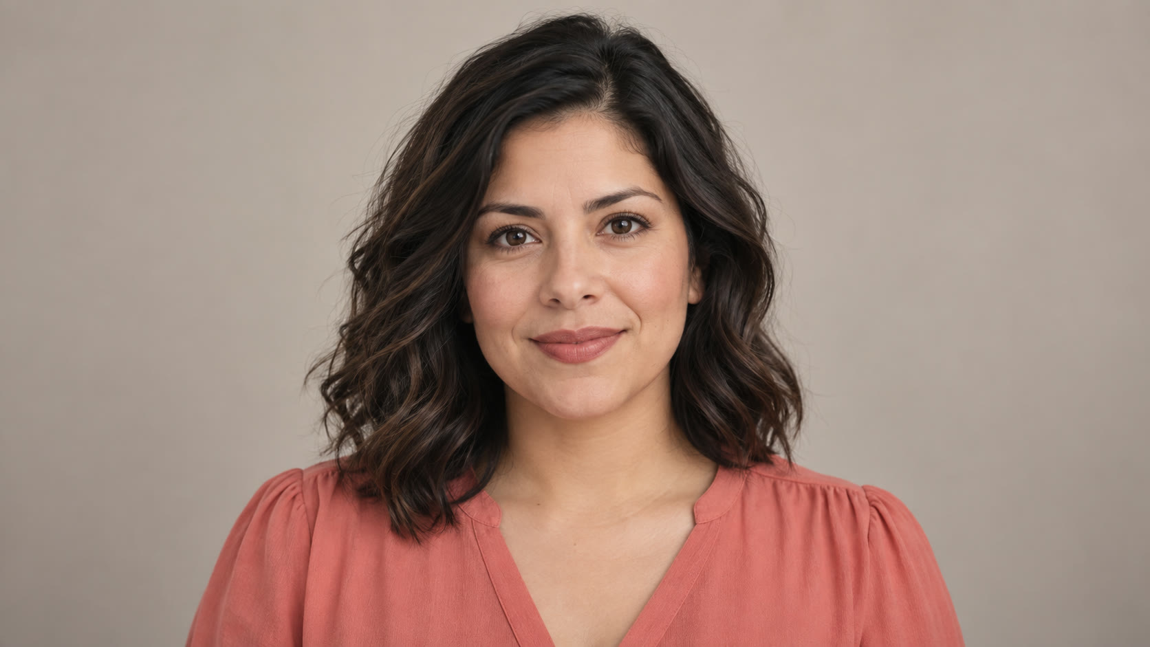 Woman with wavy dark hair in a coral blouse